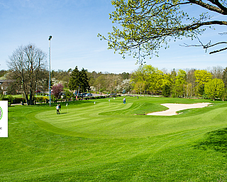 Golfplatz mit Übungsbereich Weite Ansicht eines Golfplatzes mit Spielern und Bunkern.