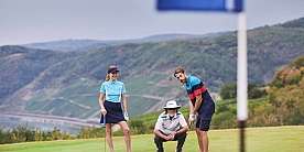 Golfspiel auf dem Grün Drei Golfer auf dem Platz, einer puttet, zwei beobachten.