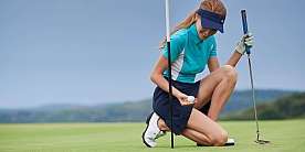 Golferin beim Putten Eine Golferin kniet und hält einen Golfball auf dem Grün.